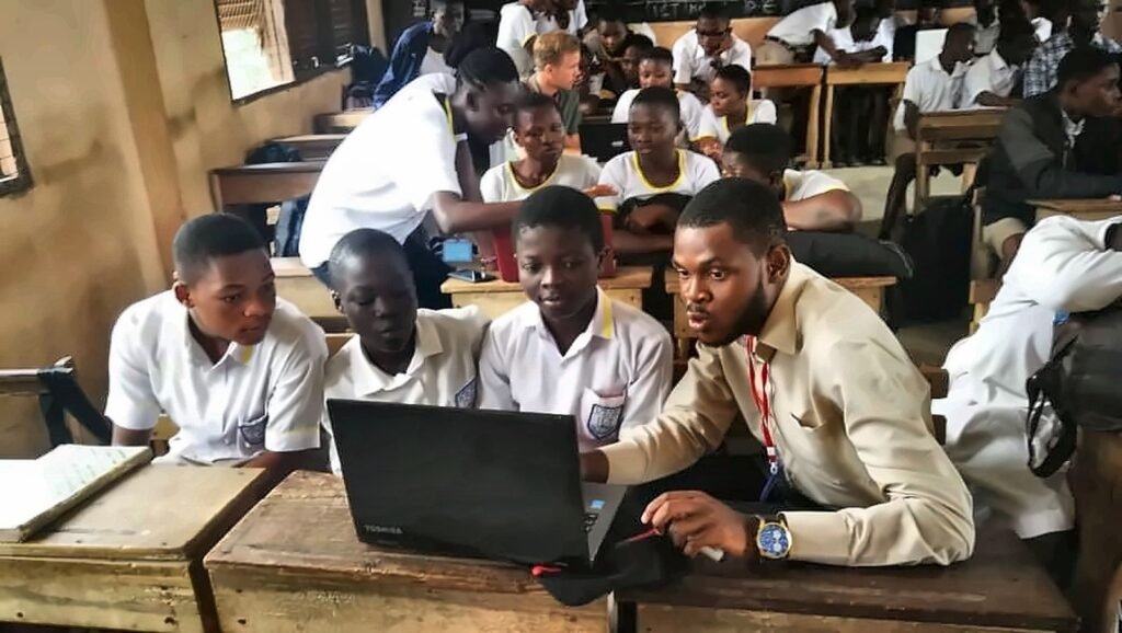 Daniel Appiah Gyekye guiding students through a laptop lesson in a classroom