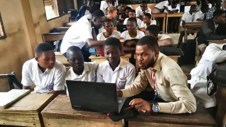 Daniel Appiah Gyekye guiding students through a laptop lesson in a classroom